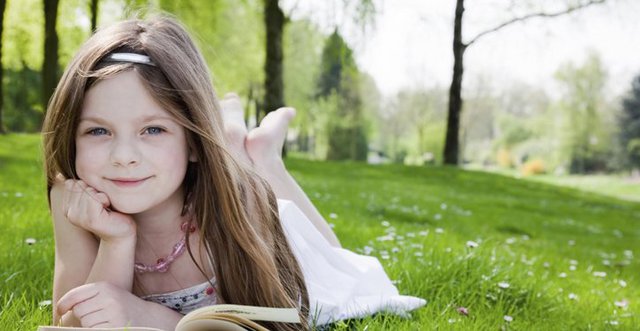Young girl lying on grass reading a book